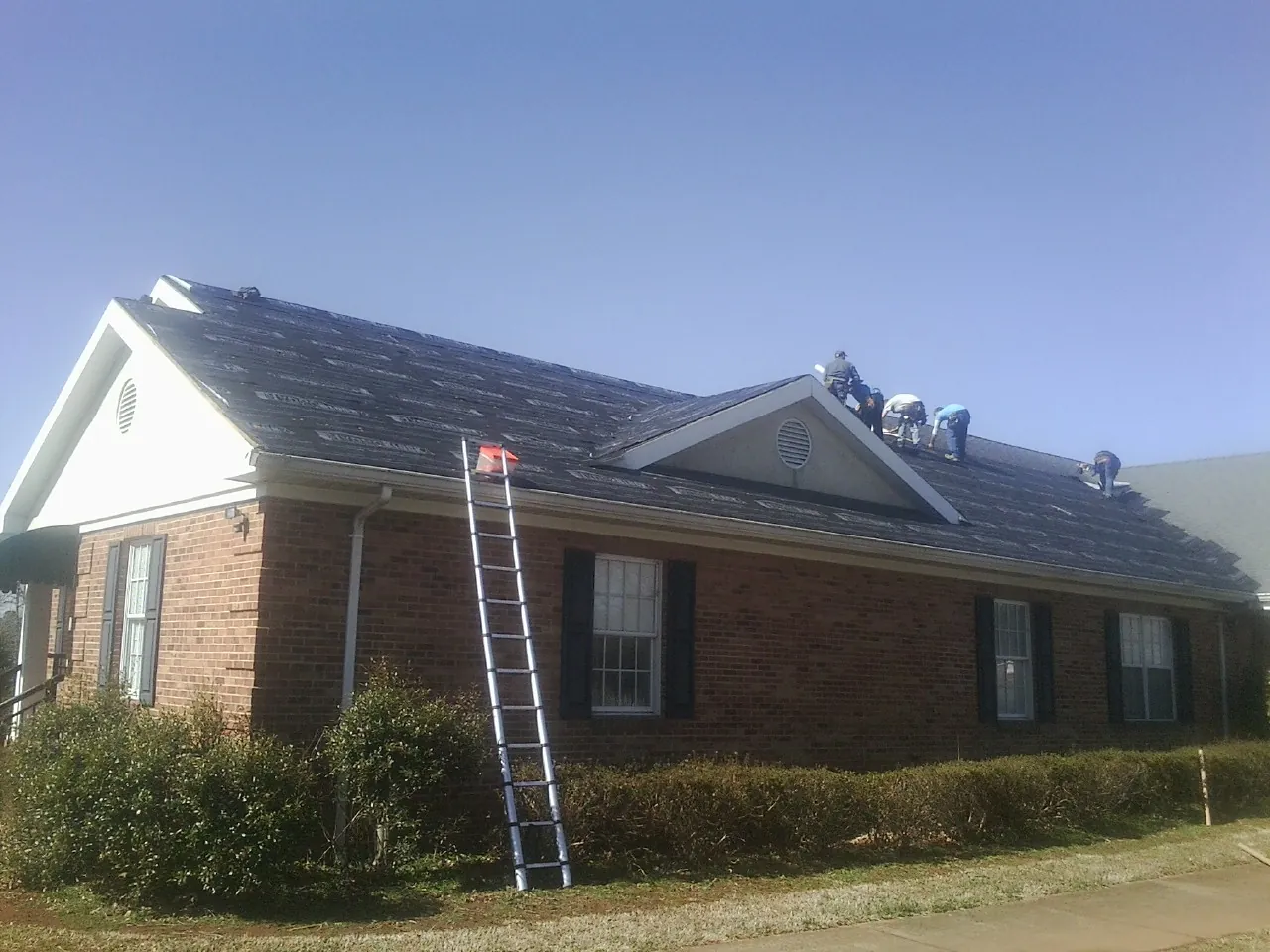 Crew tearing shingles off a brick ranch roof with a ladder set — Emergency Roof Repair work by our crew in Severn