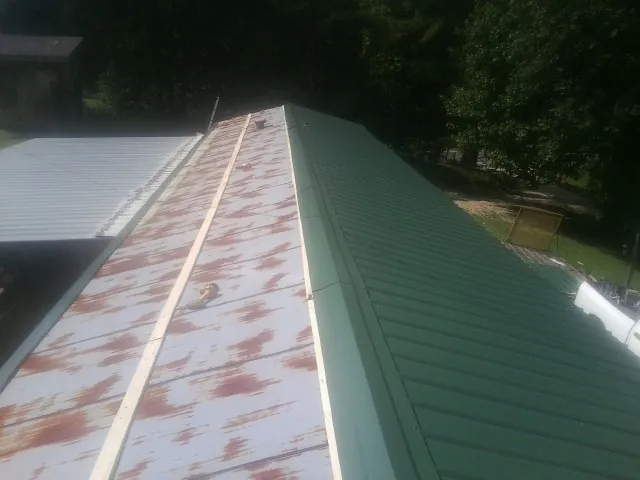 Old rusted panels beside newly installed green metal roofing — Wind Damage Roof Repair by Roofing Brothers in Severn